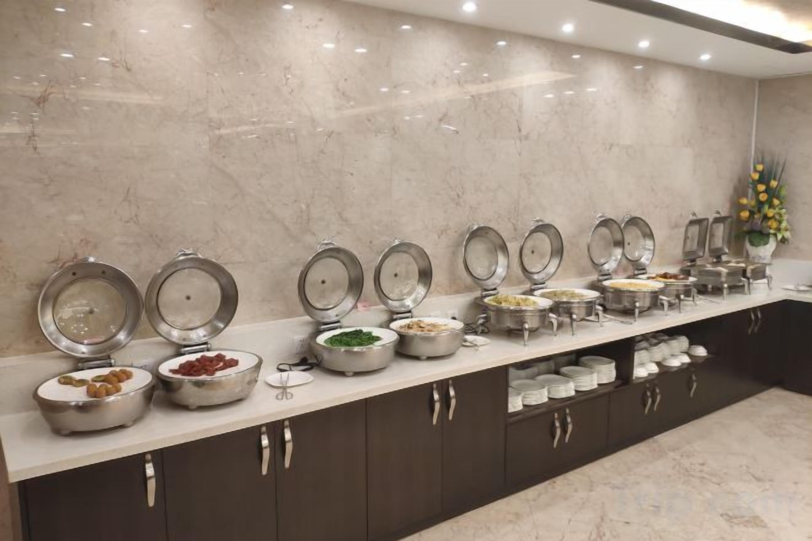 A buffet setup with multiple serving stations, each with a lid and a bowl containing various food items.