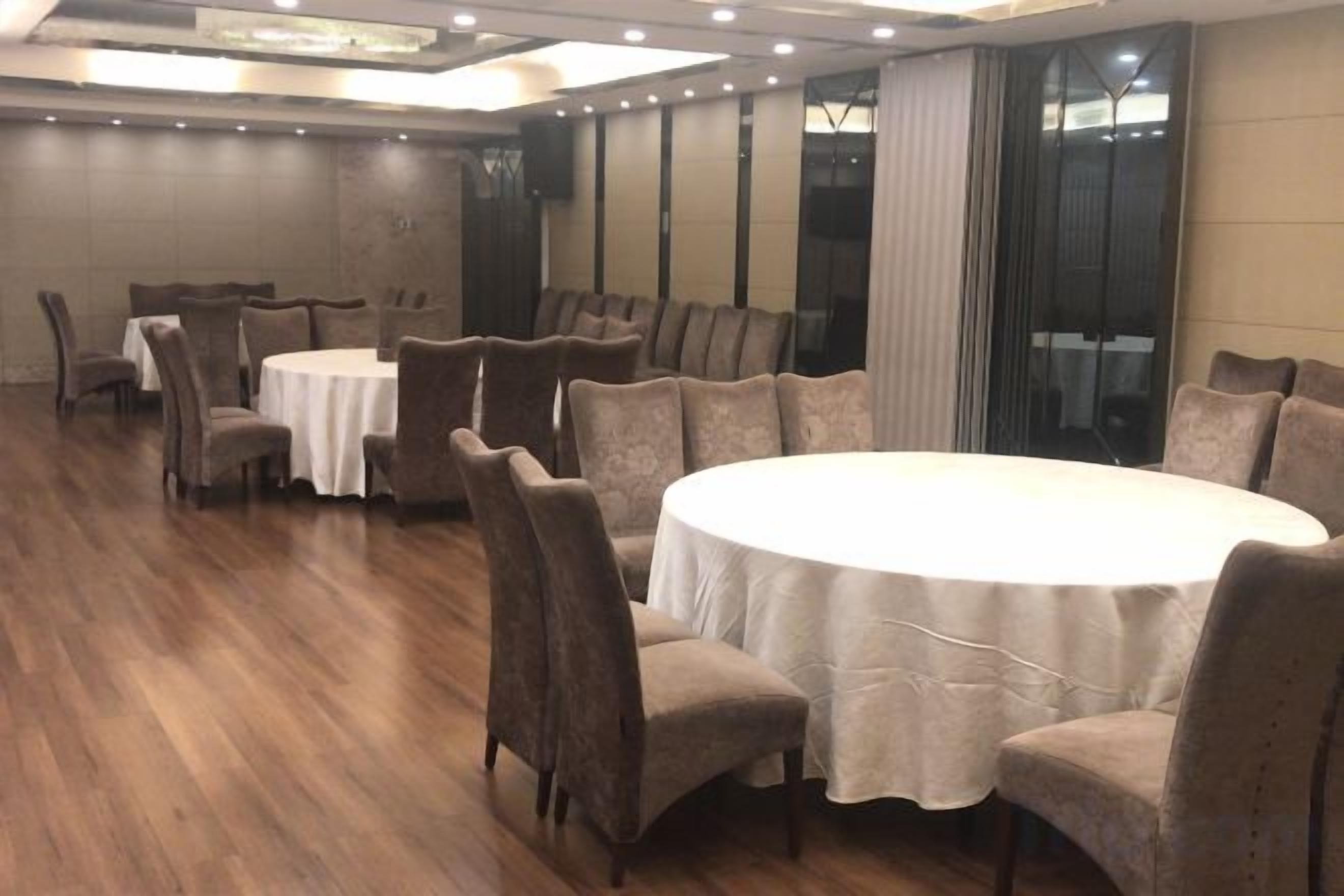 A conference room with round tables and chairs, a wooden floor, and a large window with curtains.