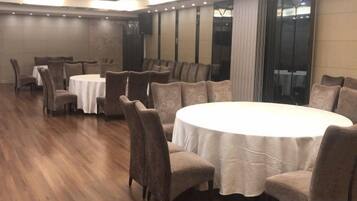 A conference room with round tables and chairs, a wooden floor, and a large window with curtains.