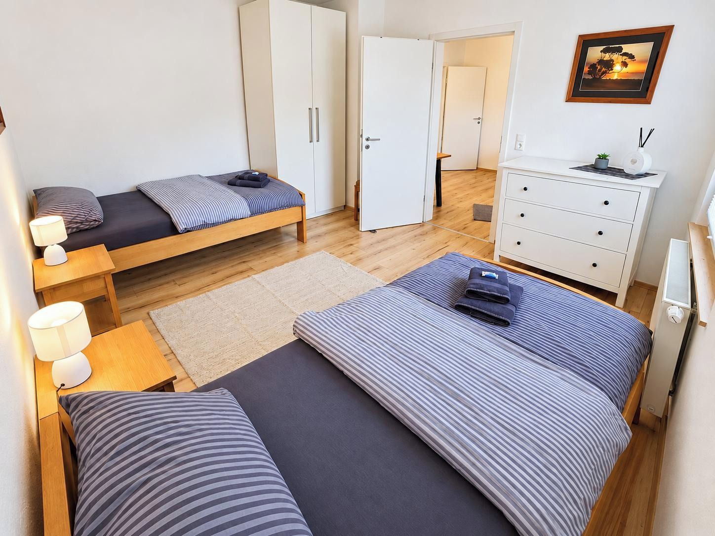 A compact bedroom with a bed, bedside tables, a wardrobe, and a dresser.