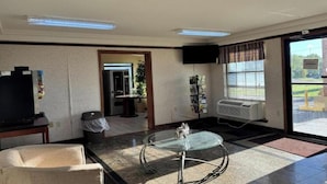 A hotel room with a television, a glass coffee table, a sofa, a trash bin, a magazine rack, and a window with blinds. - 2 Queen Bed | Smoking (Forest City, AR)