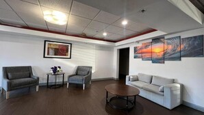 A modern interior with a gray sofa, two armchairs, a coffee table, and a painting of a sunset.
