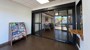A hotel lobby with a glass door entrance, a seating area with a chair, and a magazine rack.