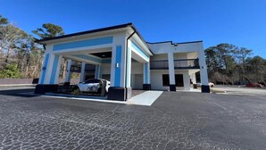 A building with a covered entrance, a parking lot, and a clear blue sky.