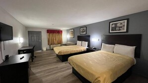 A hotel room with two beds, a desk, a chair, a TV, and a door.