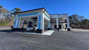 A two-story building with a covered parking area, a white car parked inside, and a clear blue sky.