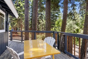 A wooden deck with a yellow table and white chairs, surrounded by tall trees. - Tahoe Lake & Mountain Retreat (Carnelian Bay)