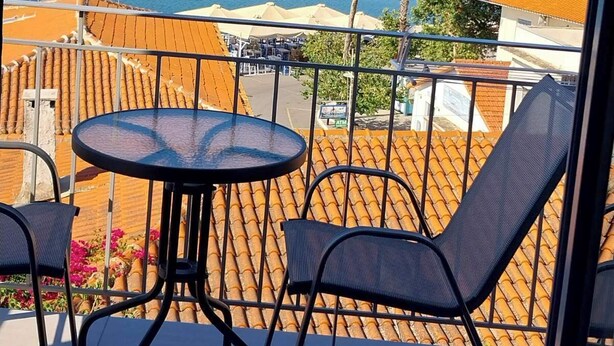 Parveke, jossa on pöytä ja tuolit, ja josta avautuu näkymä rannikkoalueelle, jossa on veneitä, sekä esteetön merinäkymä.