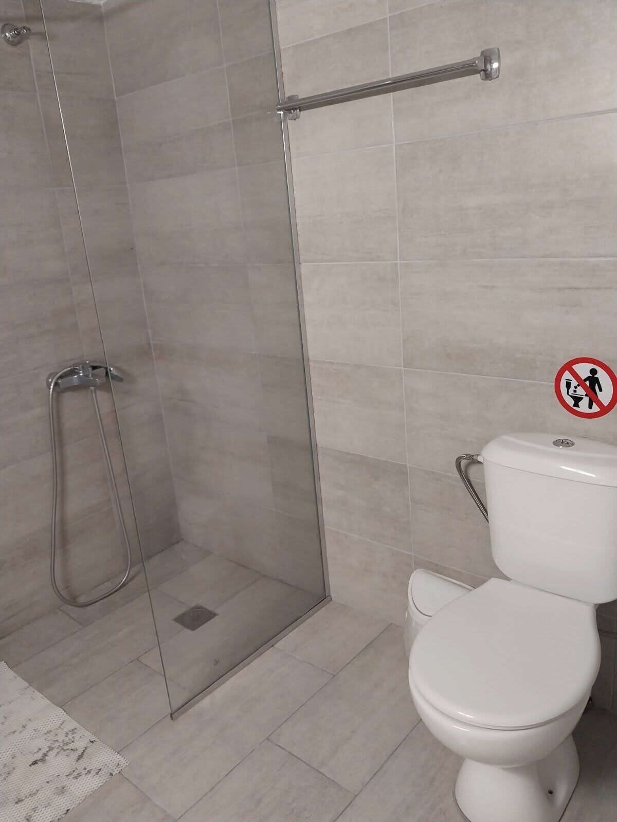 Een badkamer met een douchecabine van glas, een toilet en een bordje ‘niet roken’.