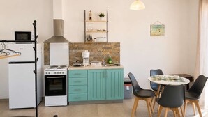 Eine kleine Küche mit Herd, Mikrowelle und Kühlschrank. Ein Essbereich mit Tisch und Stühlen ist ebenfalls vorhanden.