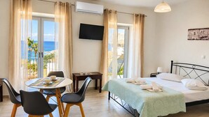 Ein Hotelzimmer mit Bett, Fernseher, Esstisch mit Stühlen und Meerblick.
