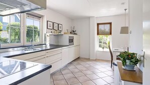 A modern kitchen with white cabinets, a black countertop, a built-in microwave, and a window with a view of greenery. - Luxury Beach Villa in Makkum with Sauna (Makkum)