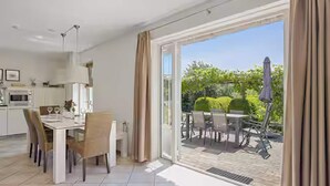 A modern kitchen with white cabinets and a dining area with a table and chairs. - Luxury Beach Villa in Makkum with Sauna (Makkum)
