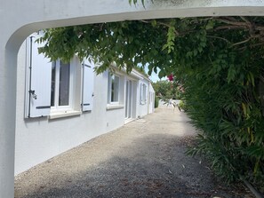 A narrow pathway leading to a row of white buildings with multiple windows, surrounded by greenery. - The Alizées Getaway (Le Château-d'Oléron)