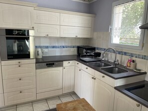 A kitchen with white cabinets, a black oven, a coffee maker, a toaster, and a sink. - The Alizées Getaway (Le Château-d'Oléron)