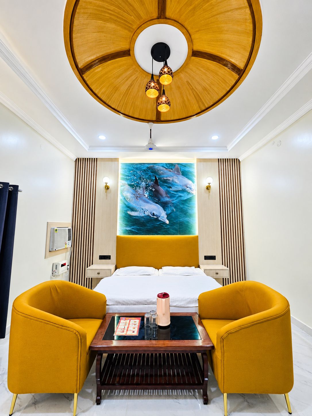 Ein Hotelzimmer mit einem Bett, zwei gelben Sesseln, einem Couchtisch, einer Deckenleuchte und einer wandmontierten Klimaanlage.