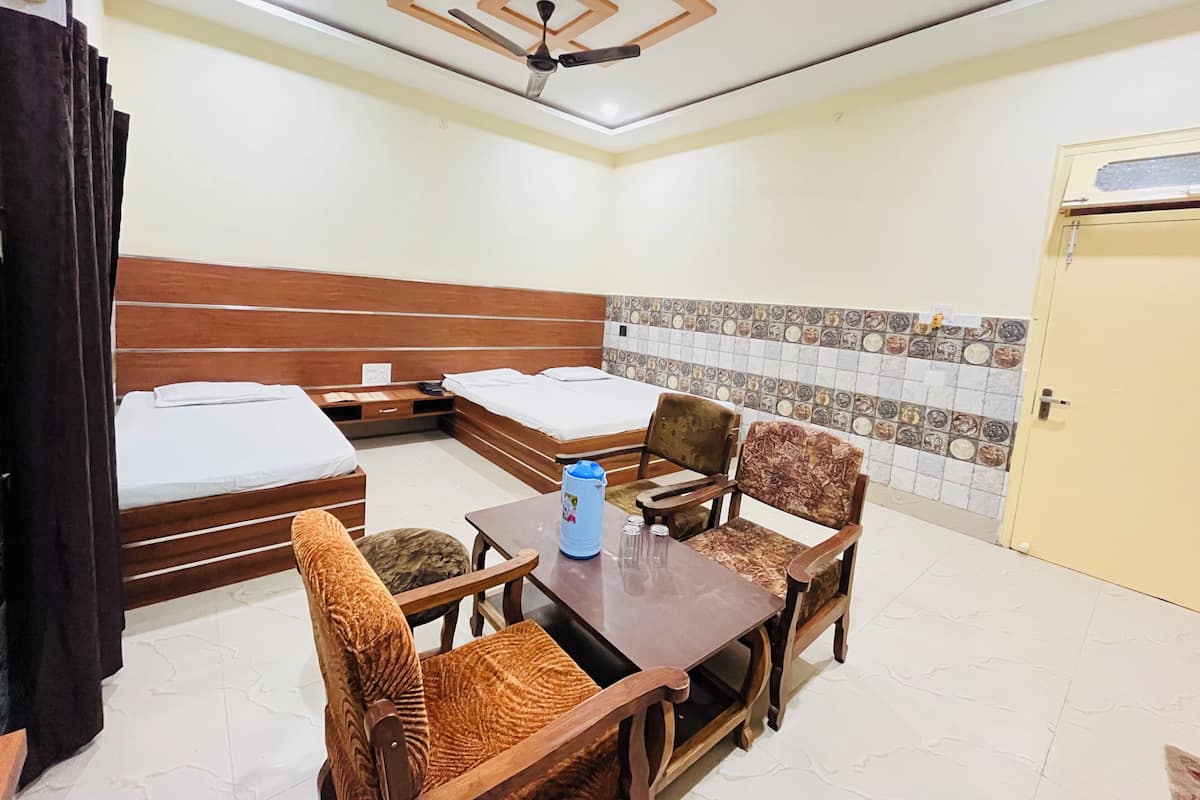 A hotel room with two beds, a wooden table, two chairs, a ceiling fan, and a tiled wall.