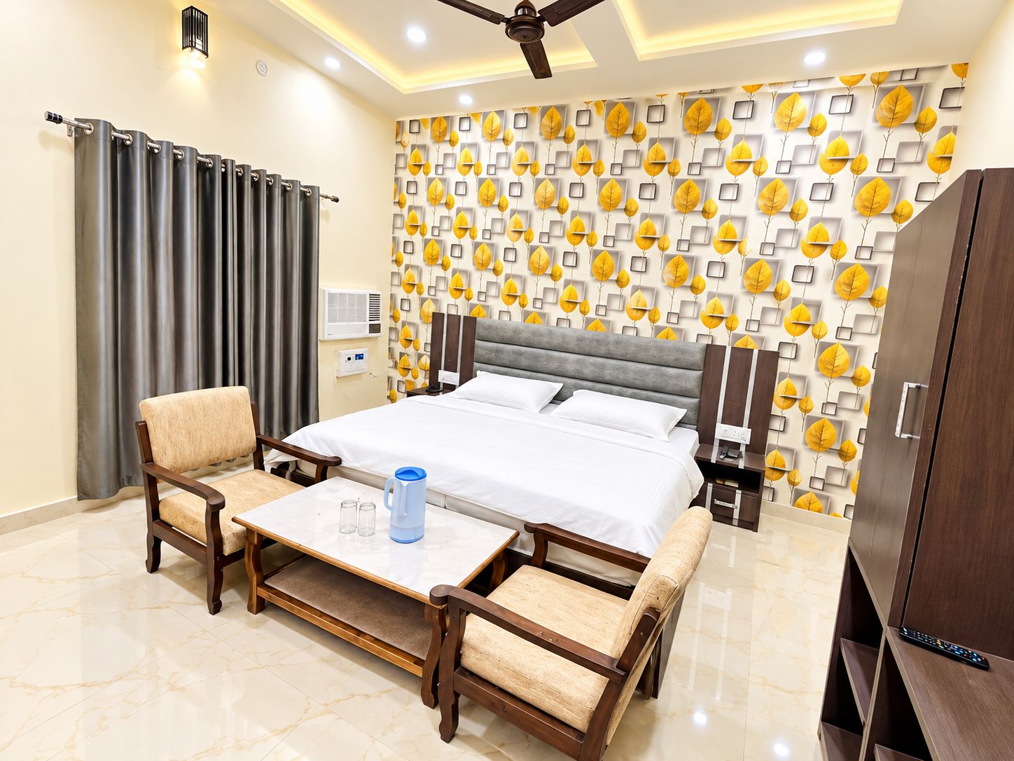 Une chambre d’hôtel comprenant un lit, deux fauteuils, une table basse, une armoire et un ventilateur de plafond.