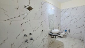 A bathroom with marble walls, a sink, a toilet, and a shower.