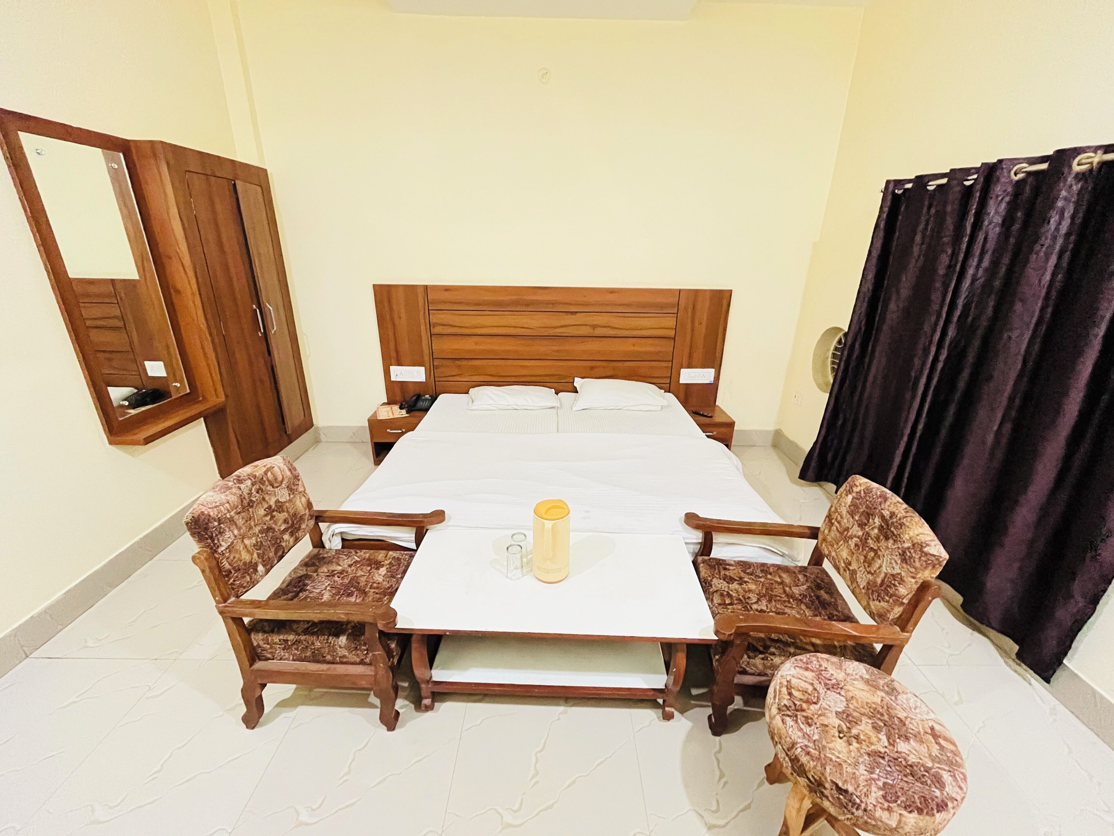 A bedroom with a wooden bed, a nightstand, a mirror, a table with a chair, and a curtain.