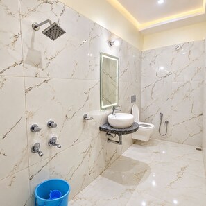 Un baño con piso de mármol, un lavamanos con espejo, una ducha y un balde azul.