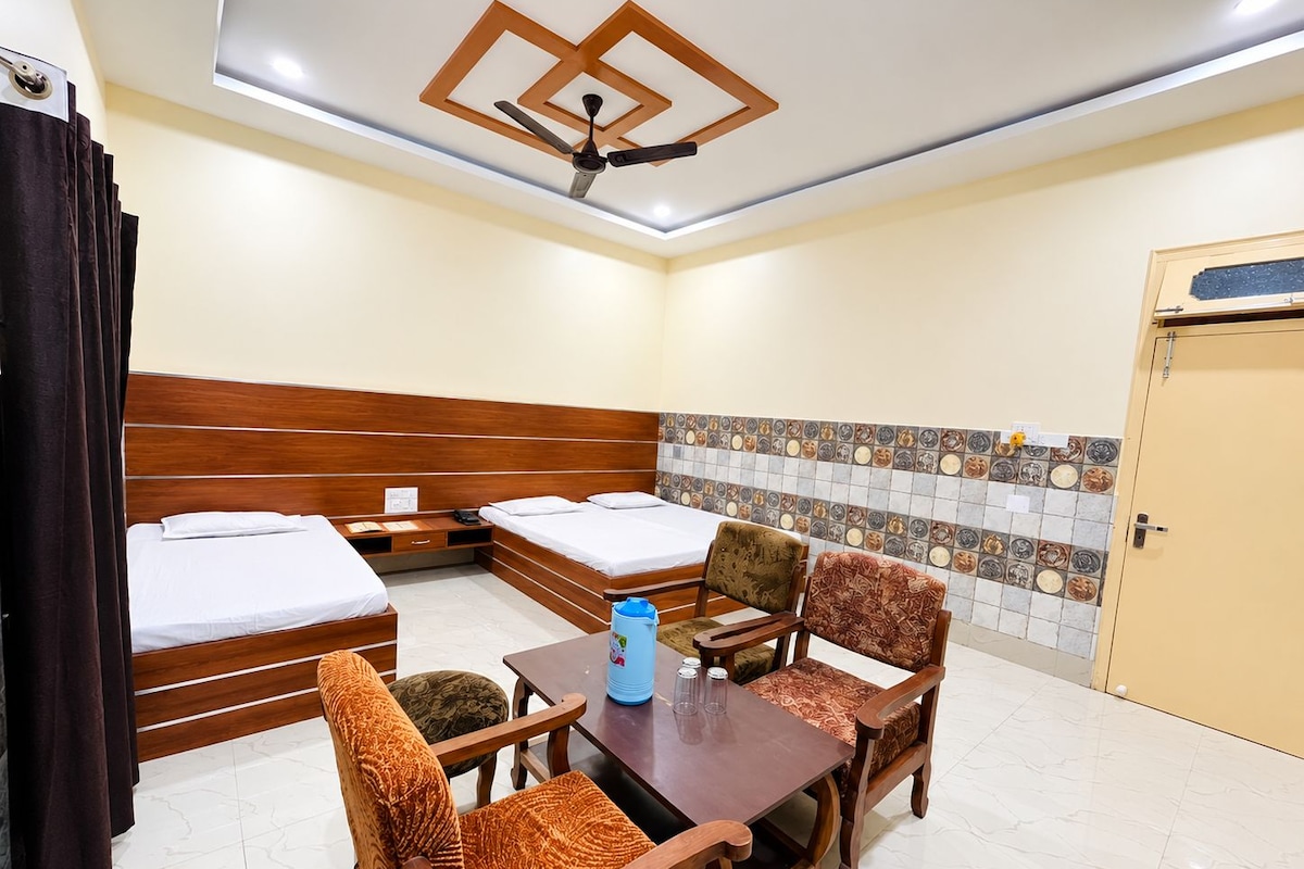 Habitación de hotel con dos camas individuales, una mesa de madera con sillas, ventilador de techo y pared de azulejos con un diseño decorativo.