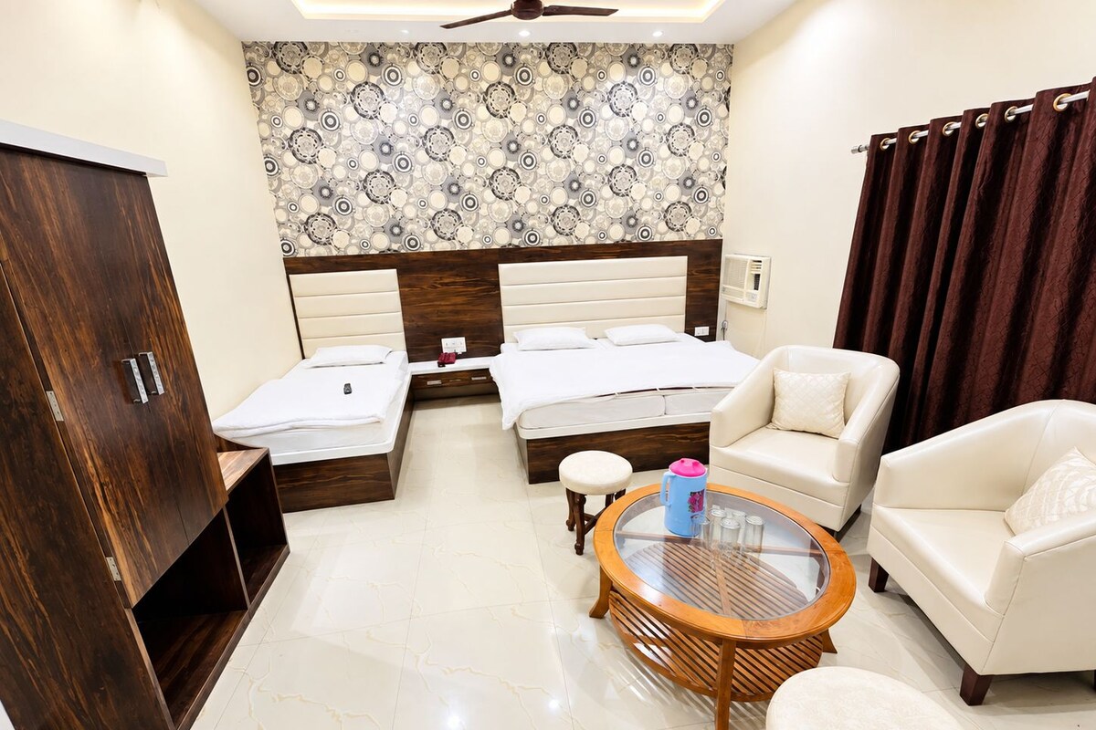 Habitación de hotel con cama, dos mesitas de noche, armario, mesa redonda de centro y dos sillones, además de un ventilador de techo.