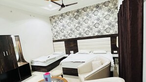 A hotel room with a bed, a sofa, a chair, a small table, a ceiling fan, and a wall with a patterned design.