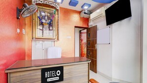 Ein Hotelrezeptionstresen mit einem 'HOTEL'-Schild, einer Wand-Klimaanlage, einem Fernseher und einem gerahmten religiösen Artefakt.