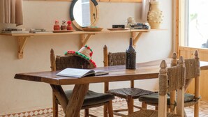 A wooden dining table with chairs, a mirror, and shelves with various items. - The Lodge (Aourir)