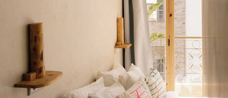 A bedroom with a bed, pillows, a wooden shelf, a framed picture, and a window with curtains.