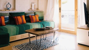 A cozy living room with a green sofa, wooden beams, a ceiling light, and a view through a glass door. - The Lodge (Aourir)