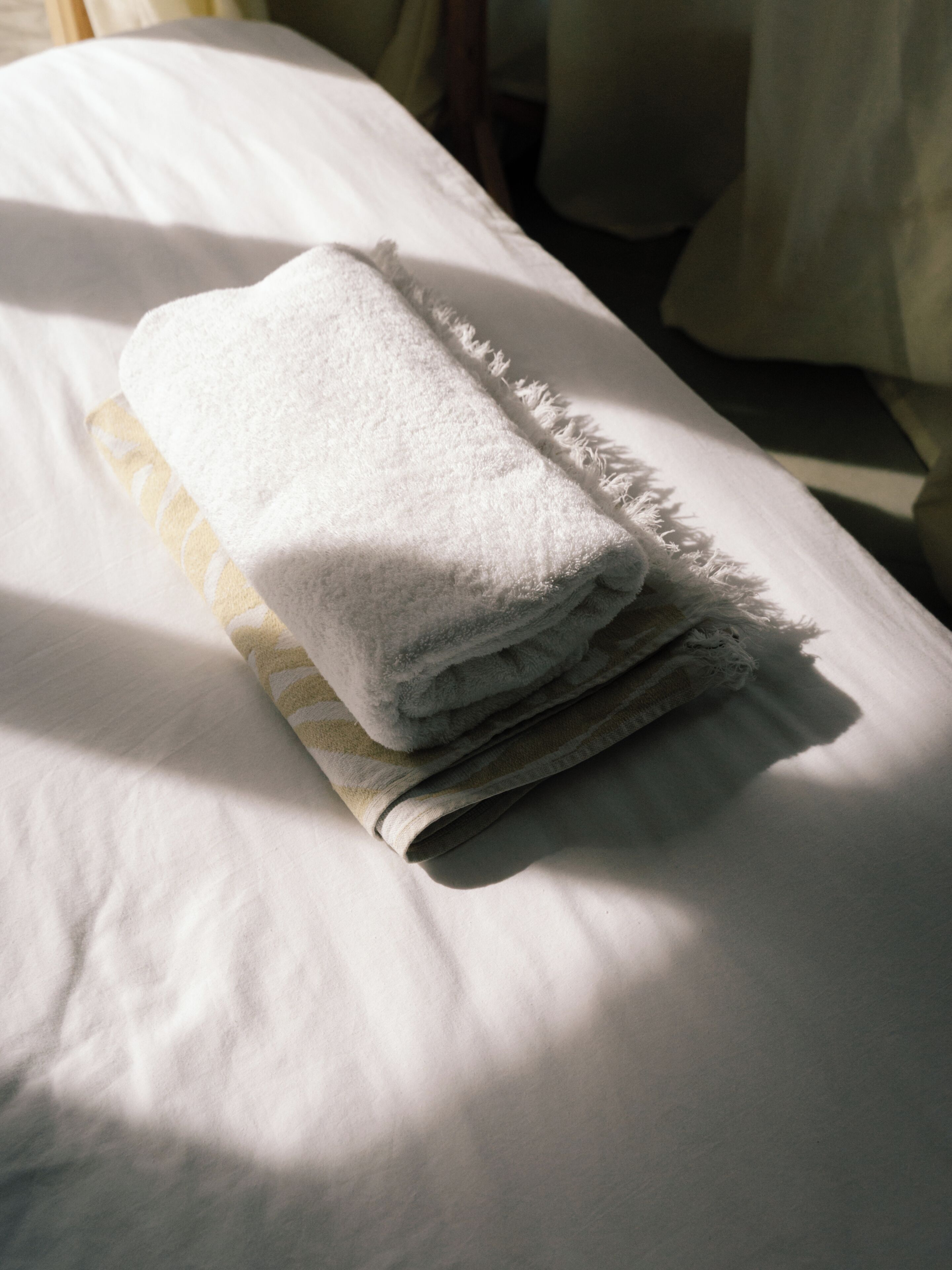 A neatly folded white towel on a bed with a patterned blanket underneath.