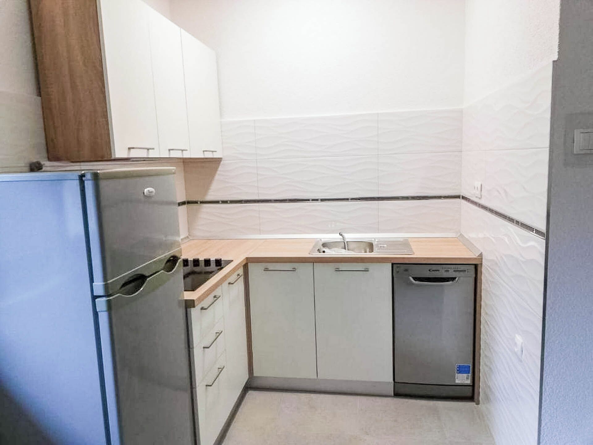 A compact kitchen with a refrigerator, stove, sink, and dishwasher.