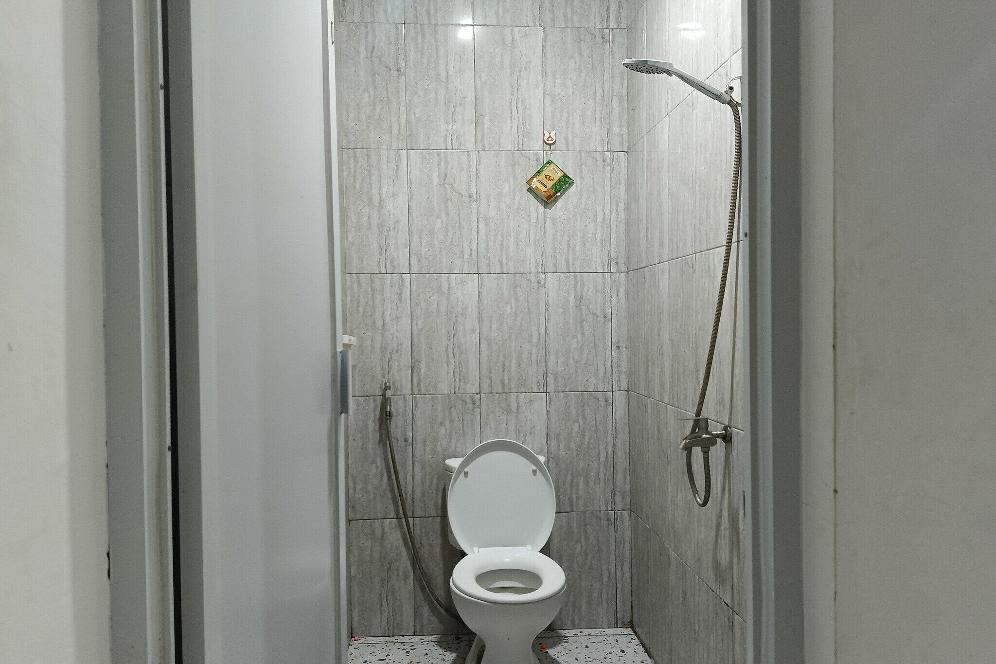 Eine kleine, geschlossene Duschkabine mit Toilette, einer Handbrause und einem am Wand montierten Wasserhahn.