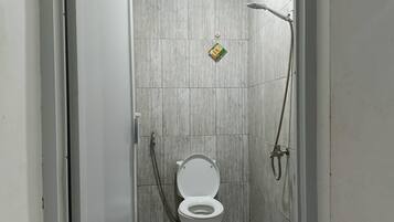 Eine kleine, geschlossene Duschkabine mit Toilette, einer Handbrause und einem am Wand montierten Wasserhahn.