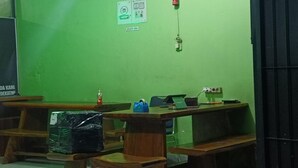 A room with green walls, a fire extinguisher, a first aid kit, and a table with a computer and a blue object. - Smart Solo Stay Near RSUD Haji (Makassar)