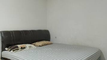 Ein Einzelbett mit karierter Bettdecke und zwei Kissen, ein dunkles Kopfstück sowie eine schlichte weiße Wand.