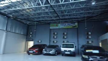 Un espace de stationnement couvert où sont garées plusieurs voitures, avec des unités de climatisation fixées aux murs et un panneau suspendu au plafond.