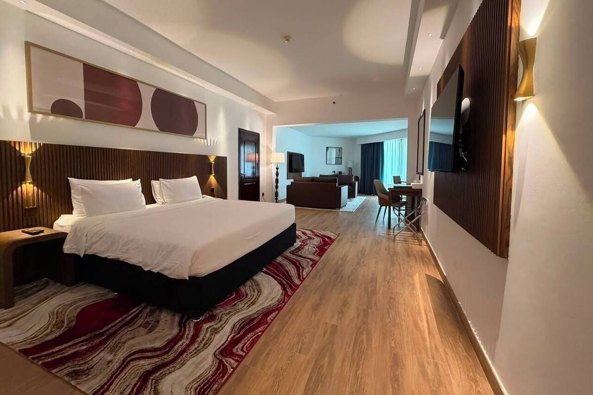 A modern hotel room with a large bed, a desk, a chair, and a television.