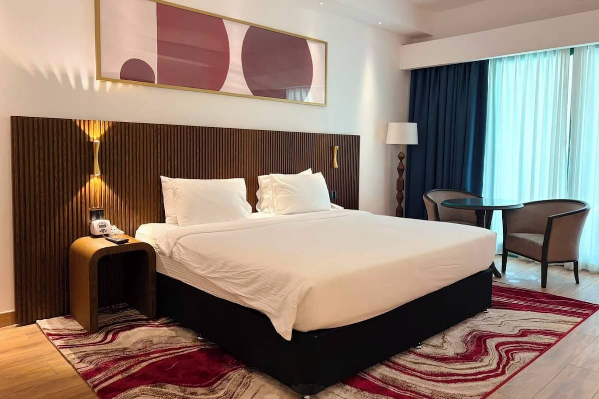 A hotel room with a large bed, a desk, a chair, a lamp, and a painting on the wall.