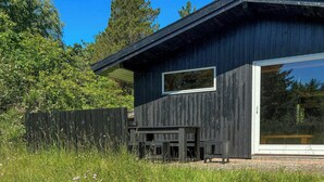 Un edifici modern de fusta amb una gran porta de vidre, envoltat per un camp d'herba i flors morades.