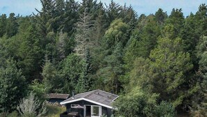 Una casa envoltada per un bosc dens, amb un cel clar a dalt.