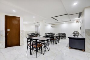 Ein Hotelzimmer mit Holztür, weißen Wänden, einem Marmorboden und mehreren Esstischen mit Stühlen.