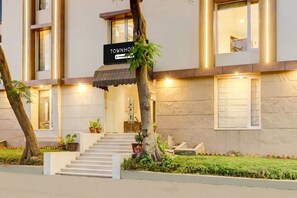 Ein mehrstöckiges Hotel mit einem Schild mit der Aufschrift 'TOWNHOUSE', einer Treppe, die zum Eingang führt, und einem gepflegten Garten.