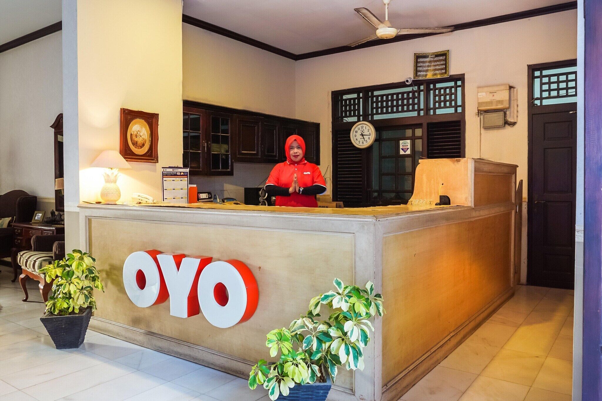 Un comptoir d’accueil avec une enseigne indiquant « OYO », une horloge et une plante en pot.