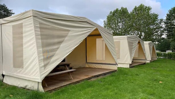 A row of beige tents with open sides, wooden benches, and a grassy area. - Cozy Coco Sweet Glamping Tent for 4 (Rijkevorsel)