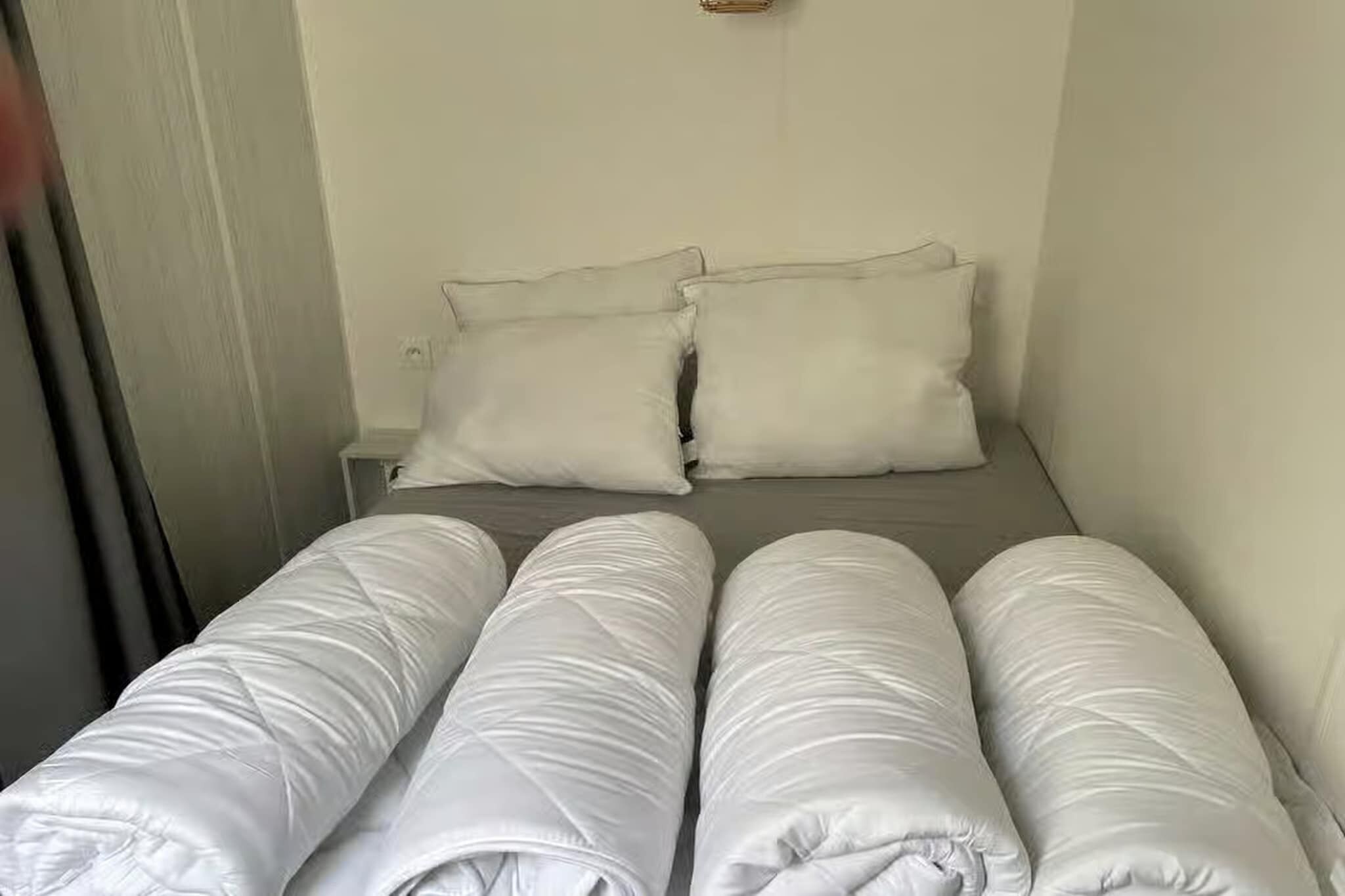 Een kleine kamer met een enkel bed, een grijs matras en witte kussens.