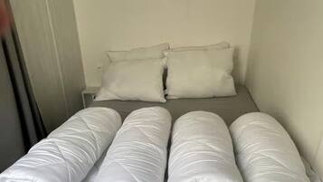 Een kleine kamer met een enkel bed, een grijs matras en witte kussens.