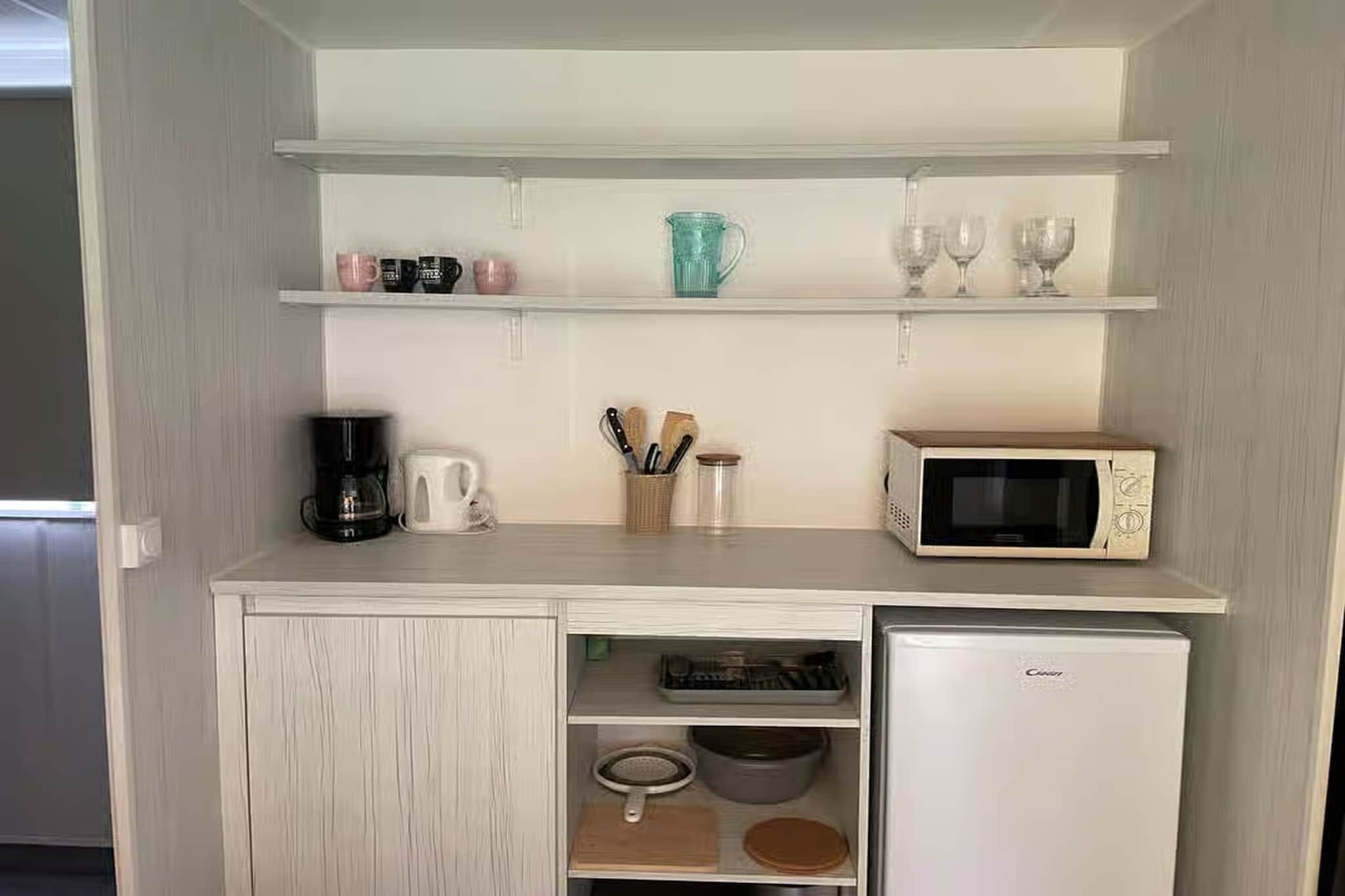 Een kleine keuken met een magnetron, koffiezetapparaat en opbergkasten.